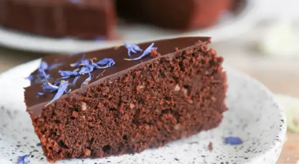 Ein Stück saftiger schokokuchen ohne zucker, garniert mit blauen Kornblumenblättern auf einem Teller.