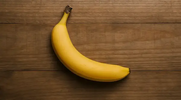 Eine einzelne, reife Banane liegt auf einem Holztisch. Sie ist gelb und leicht gekrümmt. Die Frage "wie viel Protein hat eine Banane" wird hier visuell gestellt.