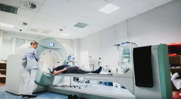 Pacjent leży na stole aparatu do scyntygrafii, podczas gdy technik przygotowuje badanie.