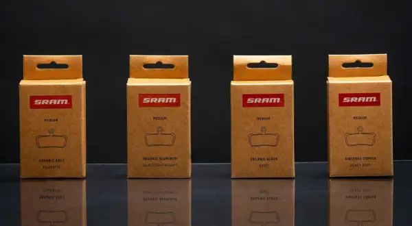 Cajas de SRAM mostrando distintos tipos de pastillas de freno: orgánicas (gris, aluminio, negra) y sinterizadas de cobre.