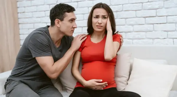 Uomo consola donna incinta con mal di testa, preoccupati per la crisi di coppia in gravidanza.