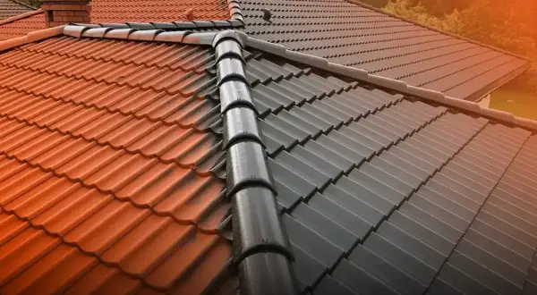Dwa kolory dachówek na dachu, z gąsiorem dachowym pośrodku. Jedna strona jest pomarańczowa, druga ciemnoszara.