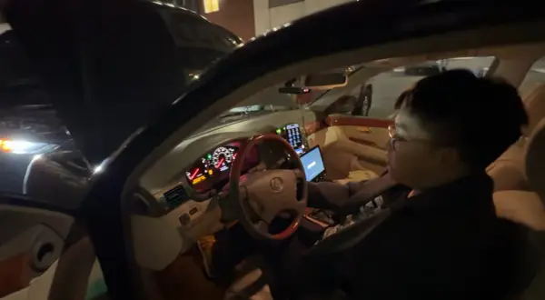 Personen försöker starta bilen som ger ett klickande ljud. Motorhuven är öppen och en laptop är ansluten till bilens system.