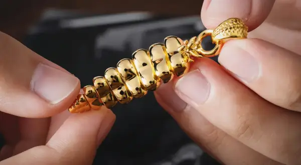 Manos sostienen un colgante dorado brillante, con forma de espiga. ¿Cómo saber si es oro? Su brillo intenso y diseño detallado sugieren autenticidad.