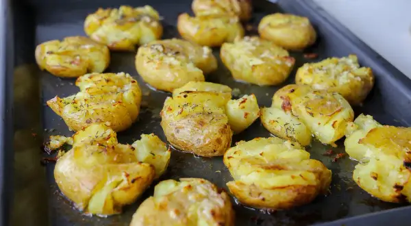Ugnsbakade smashed potatoes med ost och örter på en plåt. Krispiga och gyllene, redo att serveras.