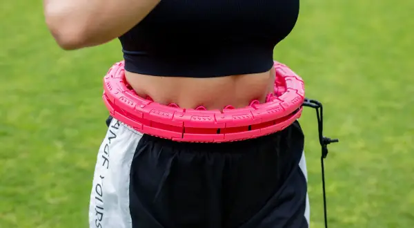 Kobieta w sportowym topie i spodenkach ćwiczy z różową obręczą. Efektywny trening silowy dla kobiet.