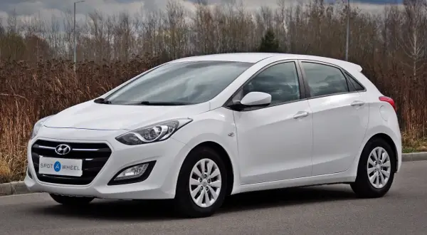 Biały Hyundai hatchback zaparkowany na drodze, z zaroślami w tle.