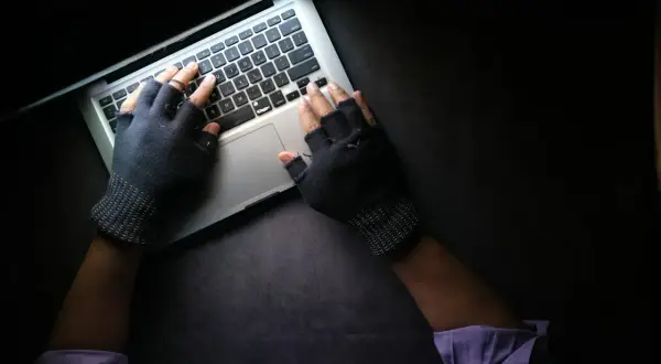 Ręce w rękawiczkach bez palców piszą na laptopie, szukając informacji, co może prowadzić do doxxingu.