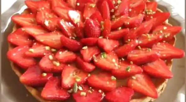 Tarte aux fraises fraîchement préparée, garnie de fraises coupées et de pistaches concassées. Un délice visuel et gustatif.