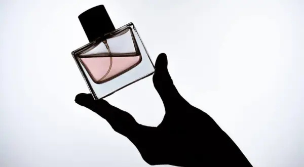 Czarna dłoń trzyma flakonik perfum z różowym płynem. To Twój **signature scent**, który podkreśla Twój styl.