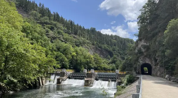 Un camino junto al río Bidasoa, con una presa y un túnel en la montaña.