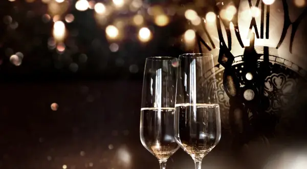 Zwei Sektgläser stehen vor einem antiken Zifferblatt. Seit wann gibt es Champagner? Seit Jahrhunderten ein Symbol für festliche Anlässe.