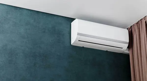 Biały klimatyzator ścienny na ciemnozielonej ścianie, obok brązowych zasłon.
