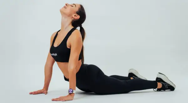 Donna in abiti sportivi neri esegue un cobra yoga, con la testa all'indietro. La sua schiena è inarcata, ma la **cattiva postura** è evidente nel collo teso.
