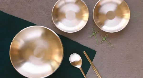 Glänzende Messingschalen, Löffel und Stäbchen auf einem Tisch. Perfekt für das Messing reinigen und eine elegante Mahlzeit.