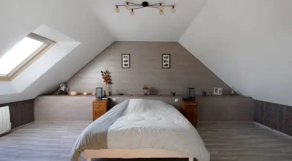 Douillette chambre mansardée avec un grand lit, une fenêtre de toit et une décoration sobre.