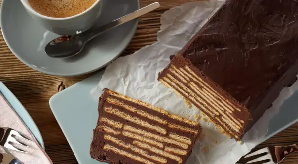 Schokoladiger kalter Hund, geschichtet mit Keksen, neben einer Tasse Kaffee.