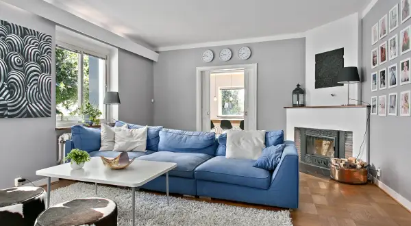 Blau passt toll zu seidengrau, wie dieses Wohnzimmer mit blauem Sofa, Kamin und Kuhfellhockern zeigt.