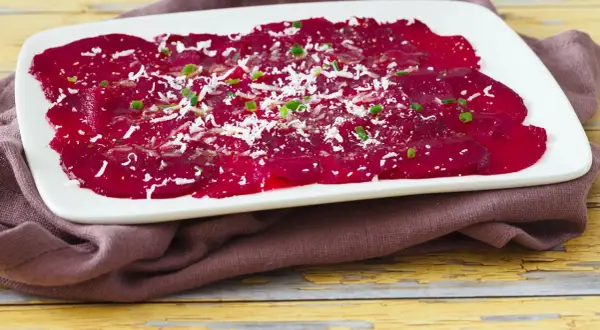Rote Bete Carpaccio, hauchdünn geschnitten und mit Parmesan und Schnittlauch bestreut, auf einem weißen Teller.