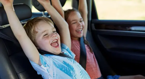 Niños emocionados en el coche, con los brazos en alto. Parecen haber alcanzado la altura mínima para no usar silla en el coche.