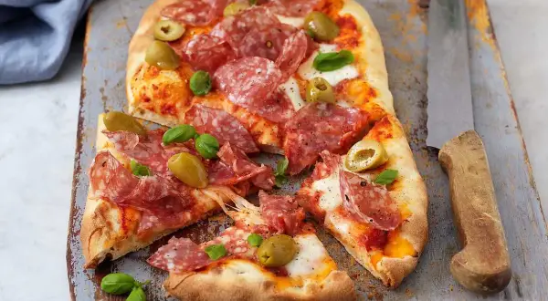 En härlig zeta pinsa med salami, oliver och färsk basilika, redo att avnjutas.