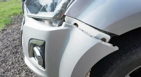 Le bouclier avant de la voiture est détaché, révélant des fixations et le pneu.