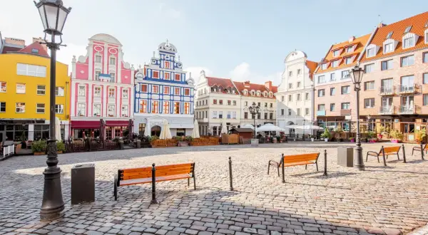 Kolorowy rynek miejski z kamienną nawierzchnią, ławkami i zabytkowymi kamienicami.