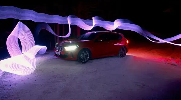 Czerwony samochód w nocnej scenerii, otoczony fioletowymi i różowymi smugami światła, efekt **panning**.
