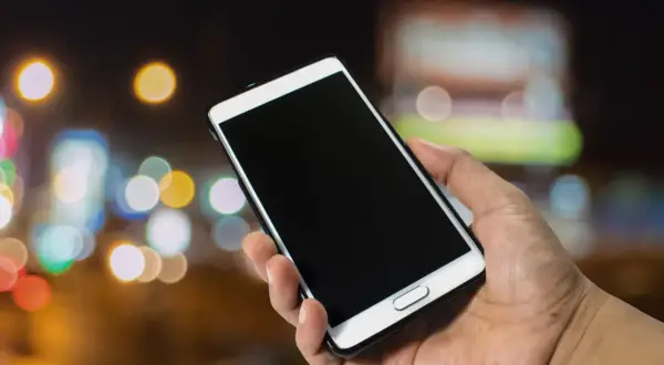 Dłoń trzyma smartfon Samsung. Dowiedz się, jak włączyć telefon Samsung, naciskając przycisk zasilania.