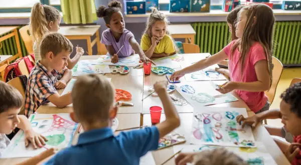 Niños y niñas disfrutan del arte en infantil, pintando con acuarelas y pinceles en una clase creativa.