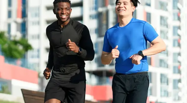 Deux hommes souriants courent ensemble dans un parc urbain. Ils semblent apprécier leur routine de courir tous les jours.