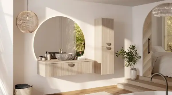 Une salle de bain moderne et chic avec un lavabo en pierre, un miroir rond lumineux et une armoire en bois clair. La lumière naturelle filtre à travers une fenêtre circulaire.