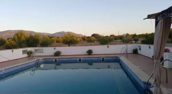 Piscina con vistas a montañas y vegetación bajo un cielo despejado.