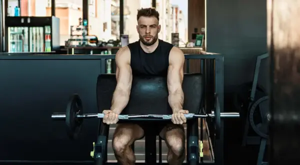 Mann trainiert Bizeps mit Langhantel im Fitnessstudio. Calisthenics-Liebhaber baut Muskeln auf.