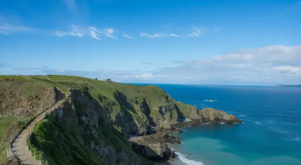 Chemin côtier verdoyant sur les falaises de Jersey, idéal pour visiter Jersey à pied. Mer bleue et ciel clair.