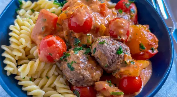 Herzhafte Hackfleisch Gerichte: saftige Hackbällchen in cremiger Tomatensoße mit Kirschtomaten und Fusilli-Nudeln, garniert mit frischer Petersilie.