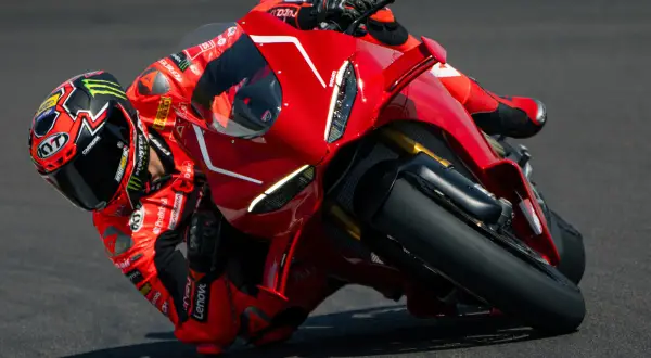 Motocyklista w czerwonym kombinezonie pochyla się na torze na swoim czerwonym Ducati Panigale V4.