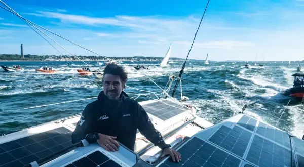 Boris Herrmann in Kiel, auf seinem Boot mit Solarpaneelen, umgeben von anderen Booten und Segelschiffen auf dem Meer.