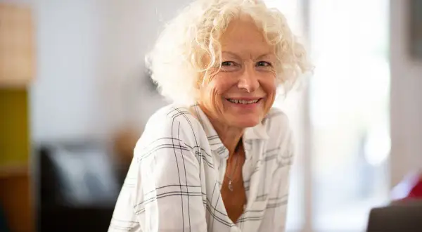 Une femme souriante aux cheveux bouclés blonds, portant une chemise à carreaux. Son état civil célibataire rayonne de joie.