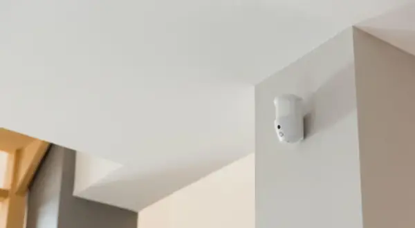 Détecteur de mouvement blanc fixé dans un coin, prêt à fabriquer une alarme.