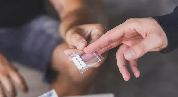 Dwie dłonie przekazują sobie małą torebkę z białymi tabletkami. To może być związane z mdma dawkowanie.