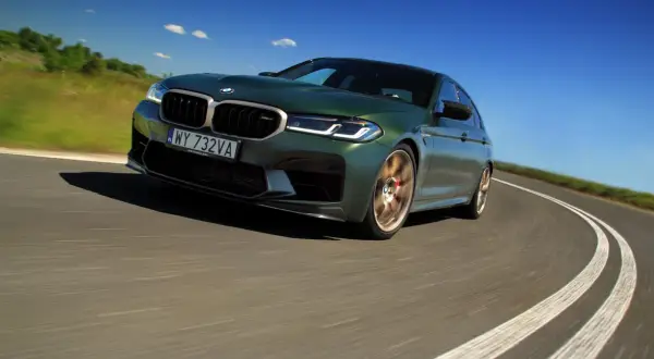 Zielony BMW M5 CS na zakręcie drogi, z rozmytym tłem i niebieskim niebem.