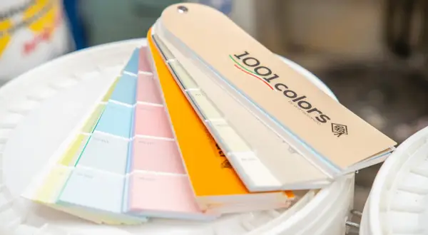 Ventaglio di campioni di colori per la tintometria, con tonalità pastello e vivaci, su secchi bianchi.