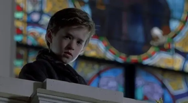 Chłopiec z filmu "Szósty zmysł" Haley Joel Osment w kościele, za nim witraż.
