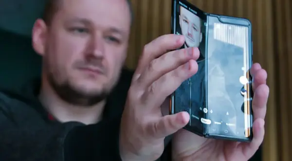 Mężczyzna trzymający składany smartfon, na ekranie którego widać jego twarz.