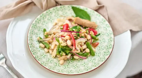 Ein bunter Thunfisch-Bohnen-Salat, italienisch inspiriert, mit grünen Bohnen, roten Zwiebeln und Tomaten auf einem Teller mit grünem Muster.