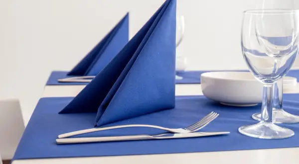 Service de table élégamment dressé avec un pliage serviette bleu vif, des couverts et des verres à vin.