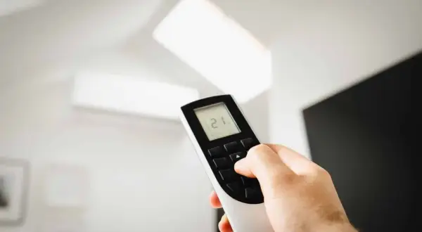 Main tenant ajuste la température de son climatiseur PAC split à 21°C avec la télécommande.