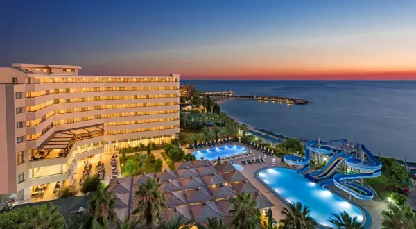 Oświetlony hotel Ozkaymak Select Resort Hotel z basenami i zjeżdżalniami wodnymi nad morzem o zachodzie słońca.