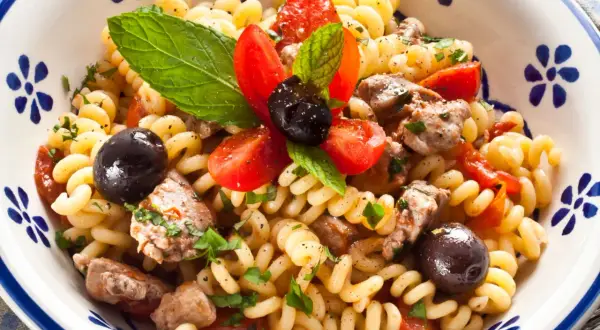 Fusilli con pesce spada, pomodorini, olive nere e menta fresca in una ciotola decorata.